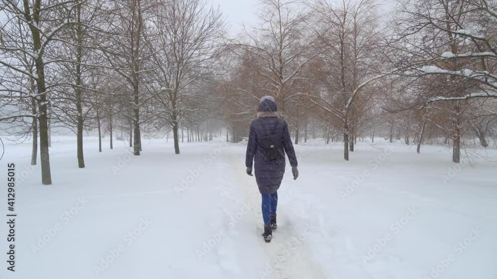 A young beautiful woman walks through the city in winter, in a heavy snowfall. The concept of the orange danger level and the warning of forecasters about the onset of heavy snowfall. A young beautiful woman walks through the city in winter, in a heavy snowfall. The concept of the orange danger level and the warning of forecasters about the onset of heavy snowfall.