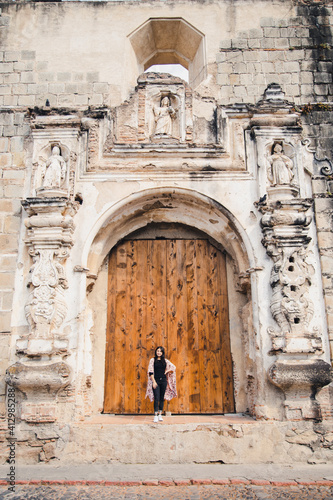 Hispanic woman standing in front of an old colonial door in a former convent in Antigua Guatemala - Baroque church ruins in colonial city © Fernanda