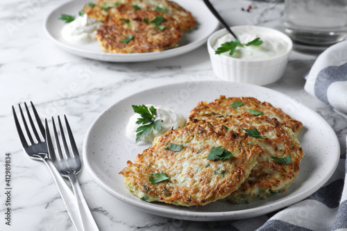 Delicious zucchini fritters served on white marble table, closeup