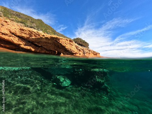 Underwater split photo from rocky sea cave formation in calm sea beach of Avlaki, Porto Rafti, Mesogeia, Attica, Greece