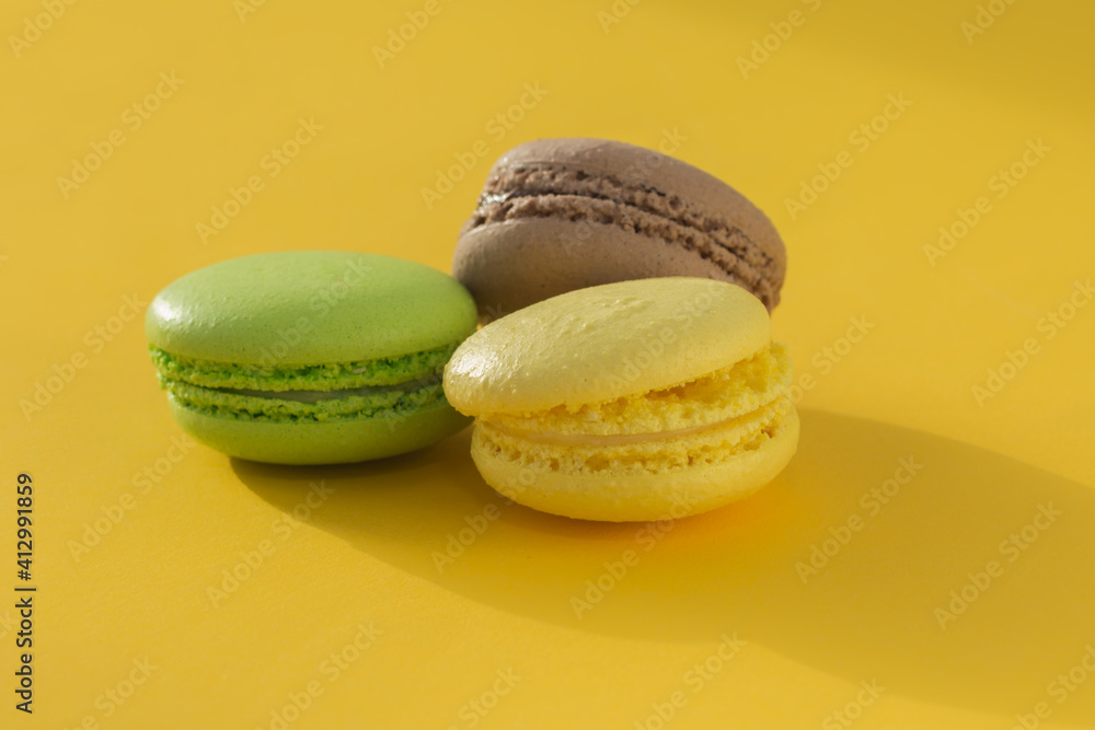 French cookies lie on a trendy yellow background. Yellow, green, brown. Macaroon. The concept is a French traditional pastry. Horizontal photo. French cookies lie on a trendy yellow background. Yellow, green, brown. Macaroon. The concept is a French traditional pastry. Horizontal photo.