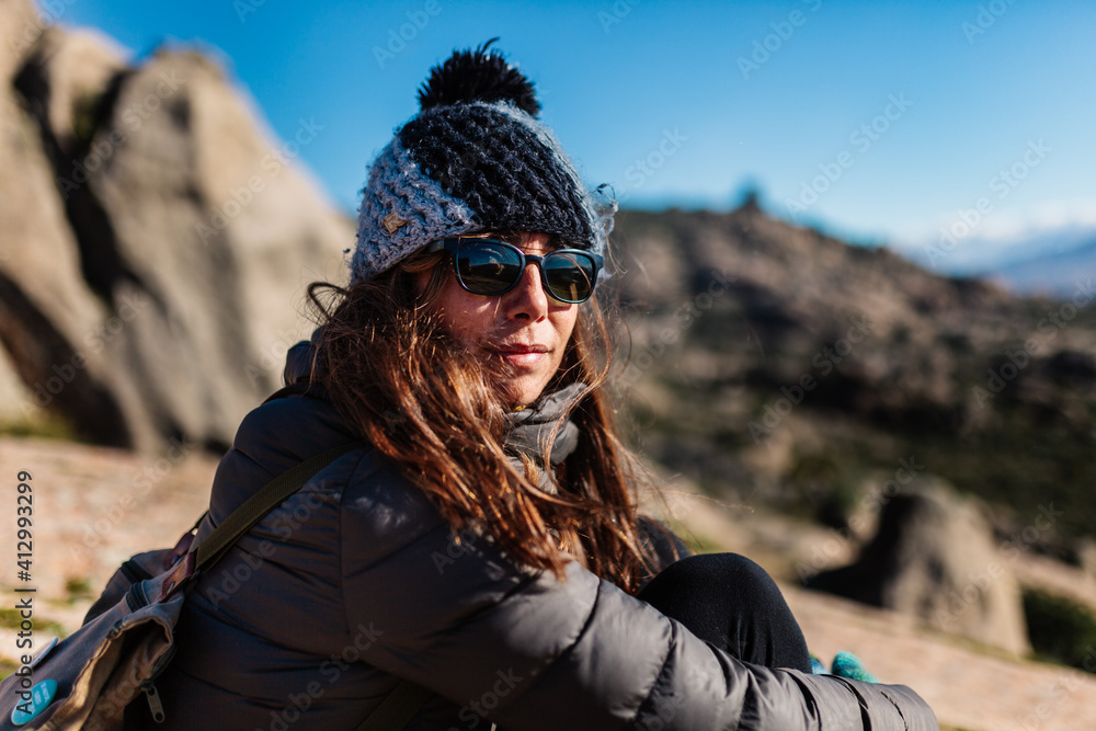 Young active woman with trekking equipment sitting, relaxing and looking at lake and mountains background