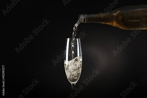 Fotografia Pouring sparkling wine from bottle into glass on black background