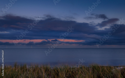 A cold winter day on Blyth Beach. Sunset with the dark blue cloudy sky with the grass in the foreground. Selective focus. Blyth, Northumberland, UK.