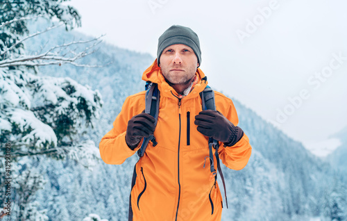 Man dressed bright orange softshell jacket with backpack have trekking on the winter mountains route. Active people or survival in the nature concept image. photo