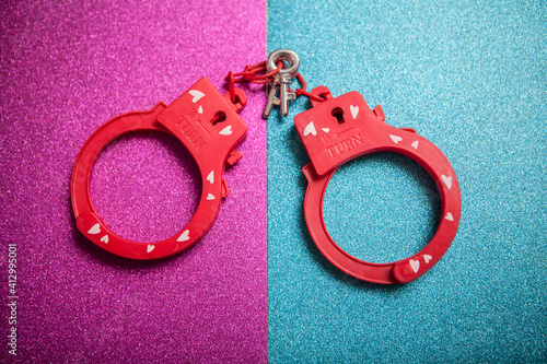 Red sex toy handcuffs on pink blue glitter background