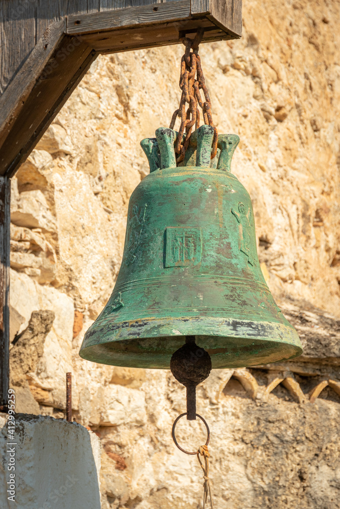 Obraz premium green copper bell on stone wall of Greek church Ekklisia Agios Ioannis hanging in the sunlight