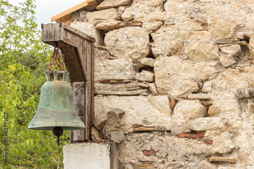 green copper bell on stone wall of Greek church Ekklisia Agios Ioannis hanging in the sunlight photo