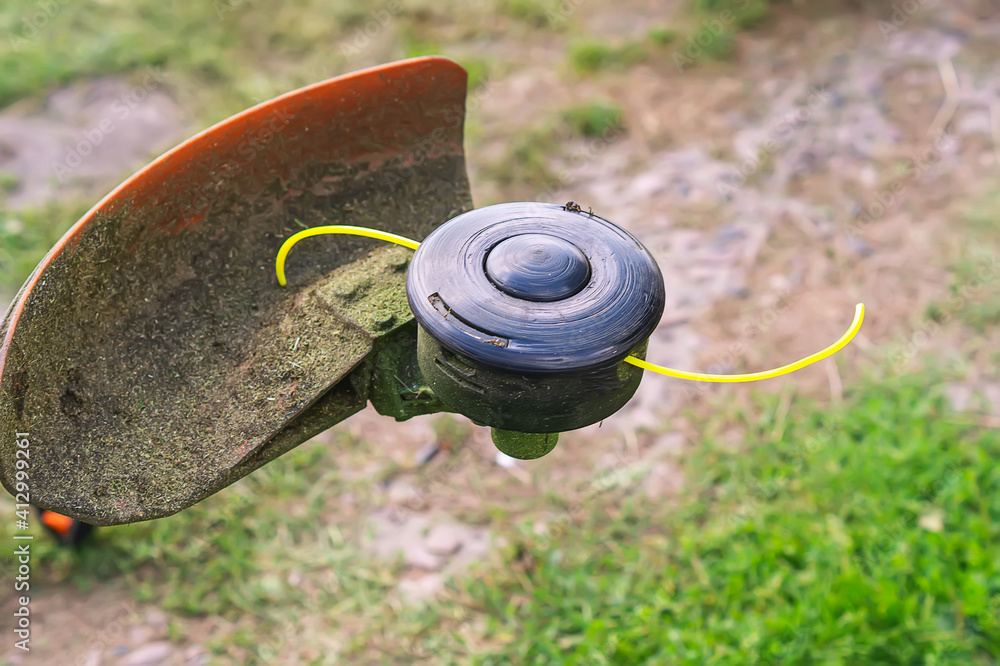 Close-up of the trimmer. A lawn mower reel with a yellow fishing
