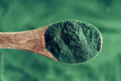 A spoonful of spirulina algae powder over a spirulina background, top view photo