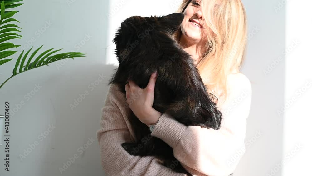 Happy young beautiful female pet owner relaxing with black mongrel dog in the white room Happy young beautiful female pet owner relaxing with black mongrel dog in the white room