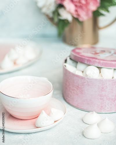 Pink box with white cookies on a light table and a coffee mug, flowers in the background