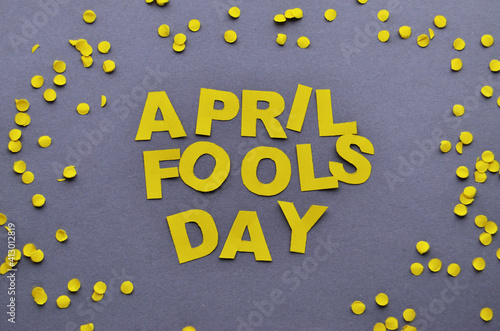 The words April Fools' Day of yellow paper are laid out inside a circle of confetti on a gray background close-up. High quality photo