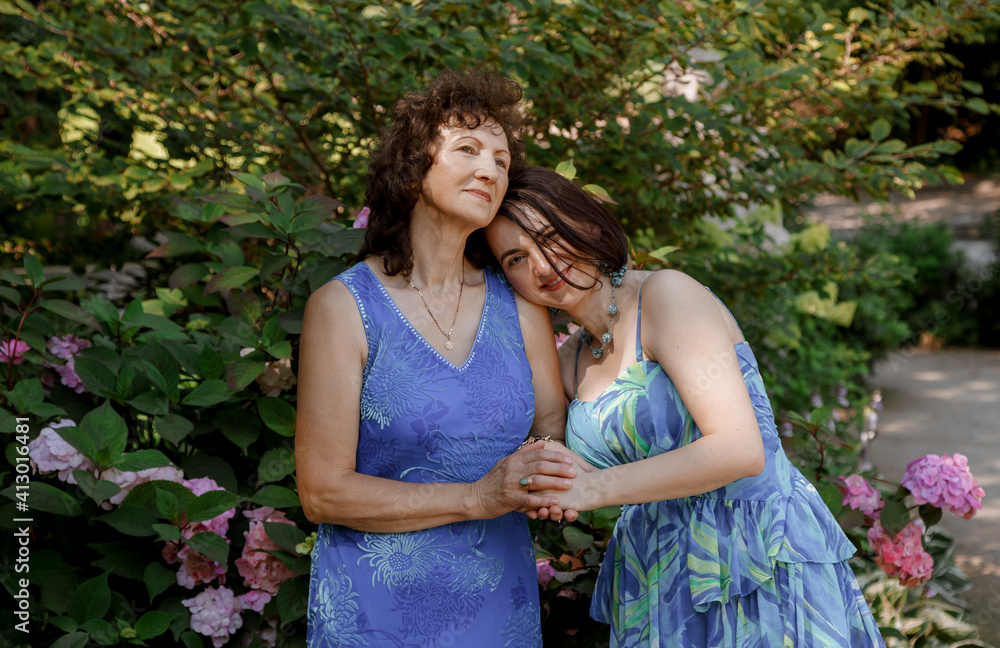 Happy woman have fun in evening gown. Mom and her daughter laughing and walking at the park. Two middle aged women chatting and looking at each other dressed in long dresses. Happy woman have fun in evening gown. Mom and her daughter laughing and walking at the park. Two middle aged women chatting and looking at each other dressed in long dresses.