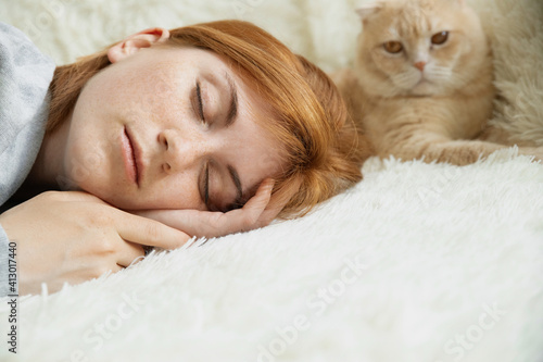 Close up pretty young red-haired female with ginger pet cat lying on bed sleeping relax in comfy bed