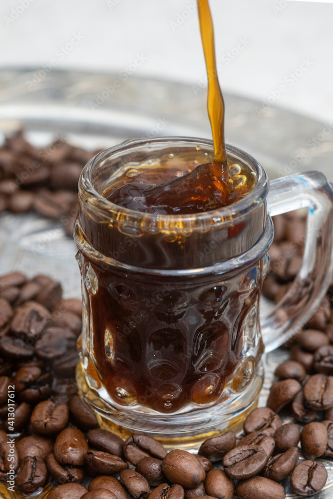 coffee being poured on a little glass, on a silver tray full of coffee beans coffee being poured on a little glass, on a silver tray full of coffee beans