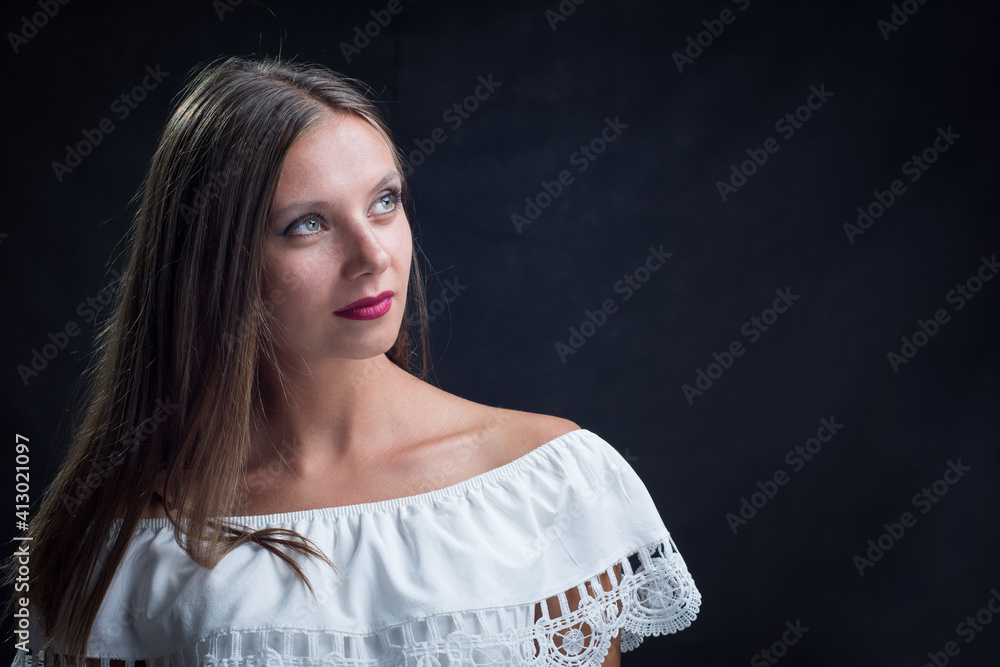 Portrait of a beautiful girl looking up in a loose white dress on a black background Portrait of a beautiful girl looking up in a loose white dress on a black background