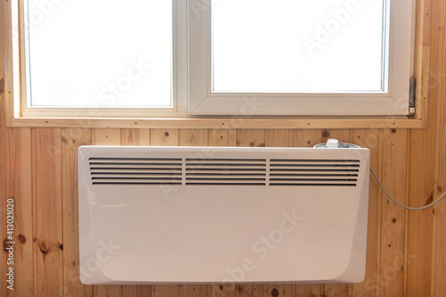 Electric radiator under the window of a country house whose walls are finished with clapboard