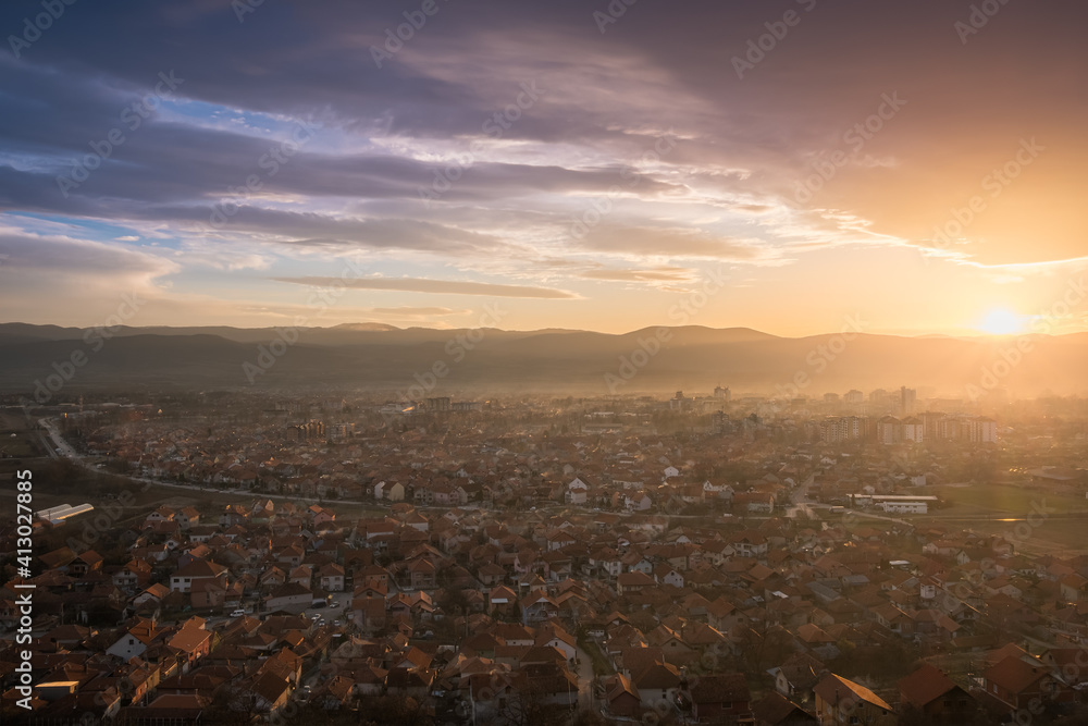 Stunning sunset view of a misty city with colorful buildings, burning sky and background horizon mountains