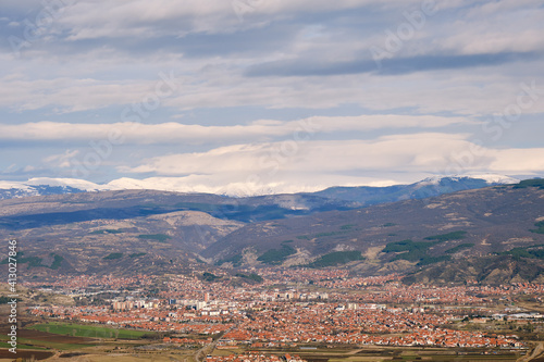 View of Pirot city from a vantage point with distant, snow capped mountain peaks in the background and cloudy sky above
