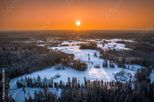 Warm sunrise over snowy countryside landscape. Pine forest covered in glowing snow. Drone aerial view. © Viesturs