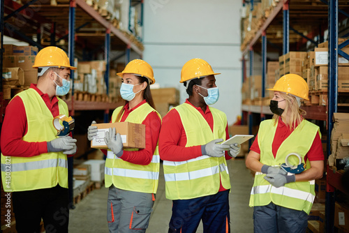 Multiracial group of warehouse workers hold delivery box, order ipad while wearing safety mask for coronavirus prevention - Focus on faces