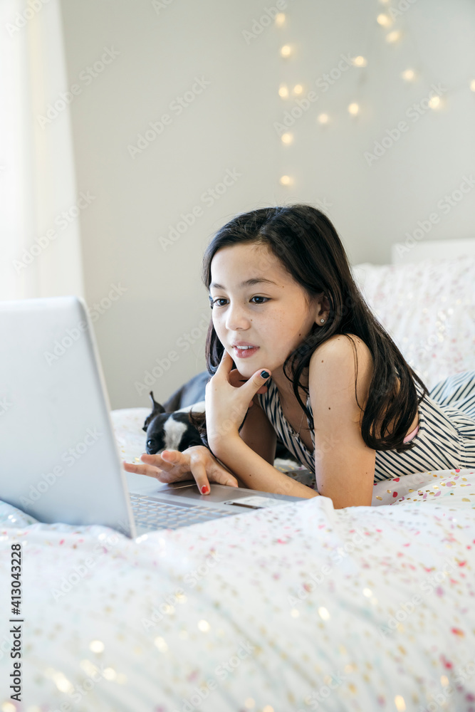 Girl laying on bed with Boston Terrier puppy home schooling on laptop computer Girl laying on bed with Boston Terrier puppy home schooling on laptop computer
