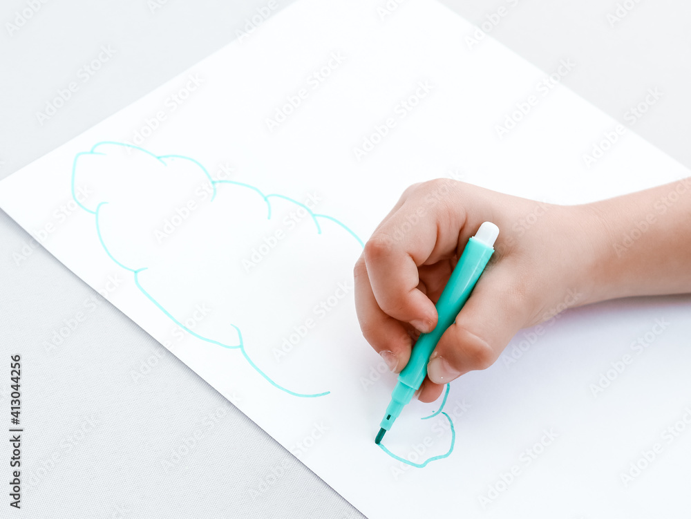 hand with pen.
Children's hand with a pen draws a cloud on a white sheet of paper, close-up side view.