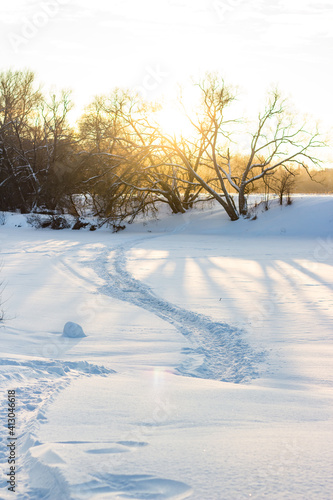 Trail on the frozen river. Sunny winter landscape on a sunny day. Snowy nature at sunset