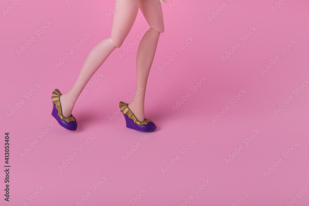 Minimal composition with female doll walking, wearing trendy shoes on pink background.