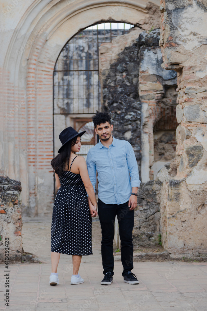 Young couple on vacation visiting famous Santiago Cathedral ruins in Antigua Guatemala - Travelers enjoying their romantic vacations - Couple holding hands looking at each other