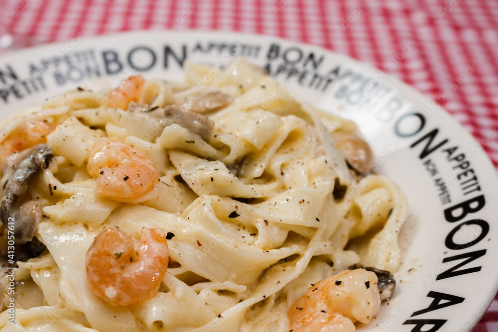 Delicious fettuccine with cream sauce of mushrooms and shrimp on a plate that says Bon Appetite with red checkered tablecloth. Delicious fettuccine with cream sauce of mushrooms and shrimp on a plate that says Bon Appetite with red checkered tablecloth.
