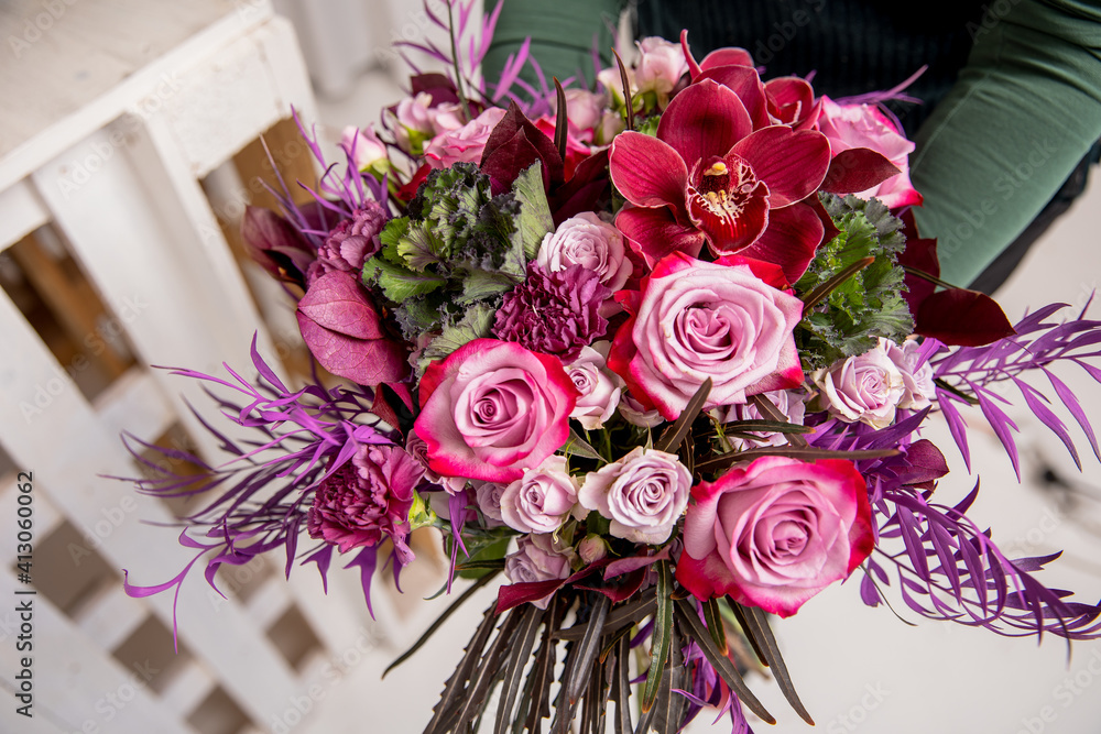 Florist's workplace in a loft space. An experienced florist composes a bouquet of roses, carnations and eucalyptus, adding flowers step by step. She is holding a ready-made bouquet in her hands Florist's workplace in a loft space. An experienced florist composes a bouquet of roses, carnations and eucalyptus, adding flowers step by step. She is holding a ready-made bouquet in her hands