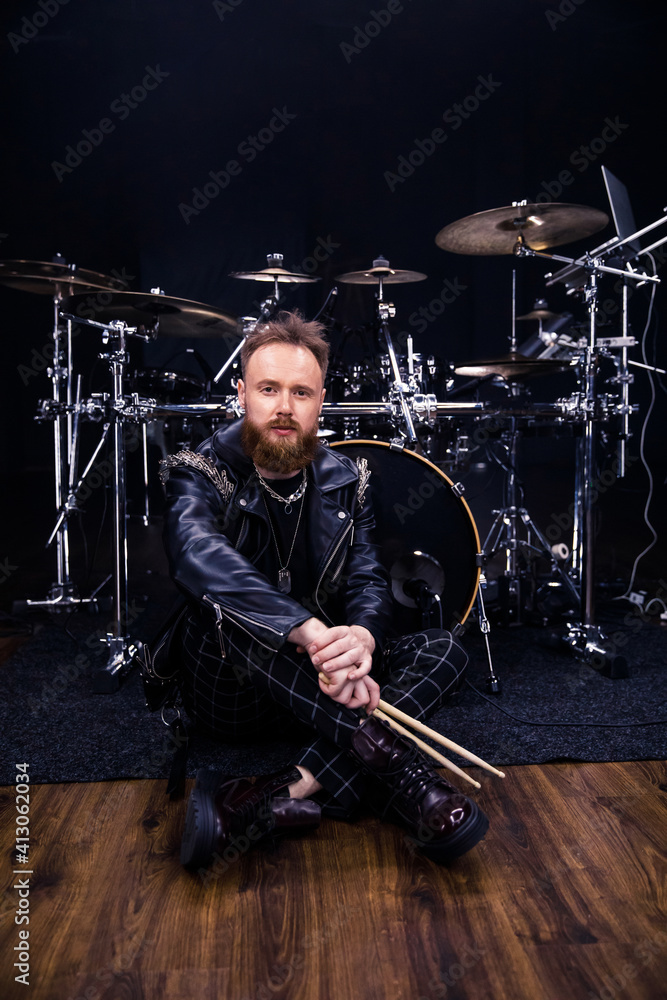 Fototapeta premium brutal portrait of a man musician with a beard and in black clothes on the background of musical instruments drums