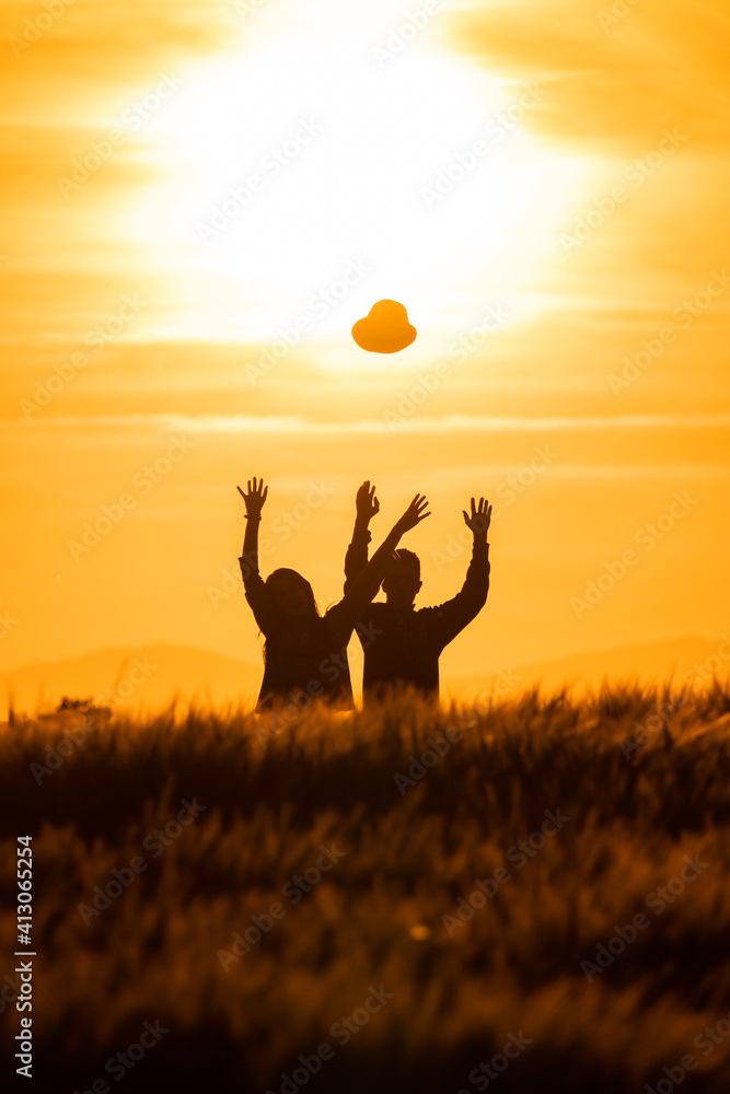 silhouette of girl and boy throwing hats in the air at sunset in the countryside