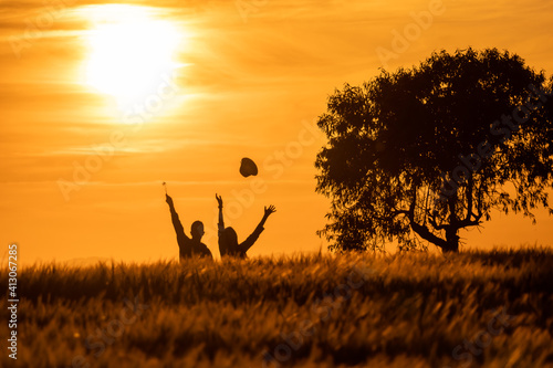 silhouette of girl and boy throwing hats in the air at sunset in the countryside © rsimona