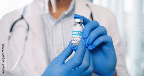 Close up shot of healthcare worker specialist in protective uniform holding in hands in gloves ampoule with coronavirus vaccine, covid-19 vaccination concept, virus cure medicament, healthcare