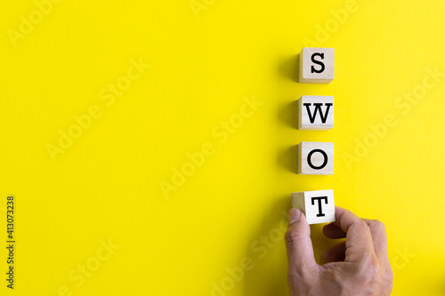 hand putting wooden cube with swot analysis on yellow background and copy space. strategy idea concept.