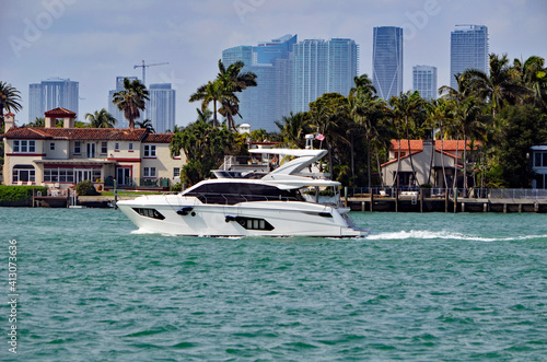 Luxury white motor yacht cruising by RivaAlto island in Miami Beach,Florida with Miami tall building skyline in the background ..