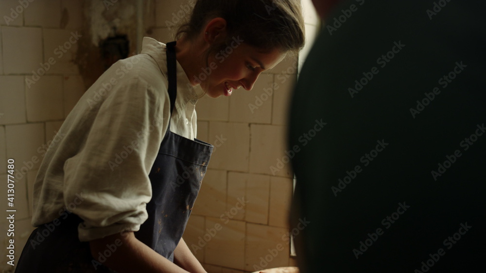 Young woman working with wet clay in pottery. Lady and man sculpting together 