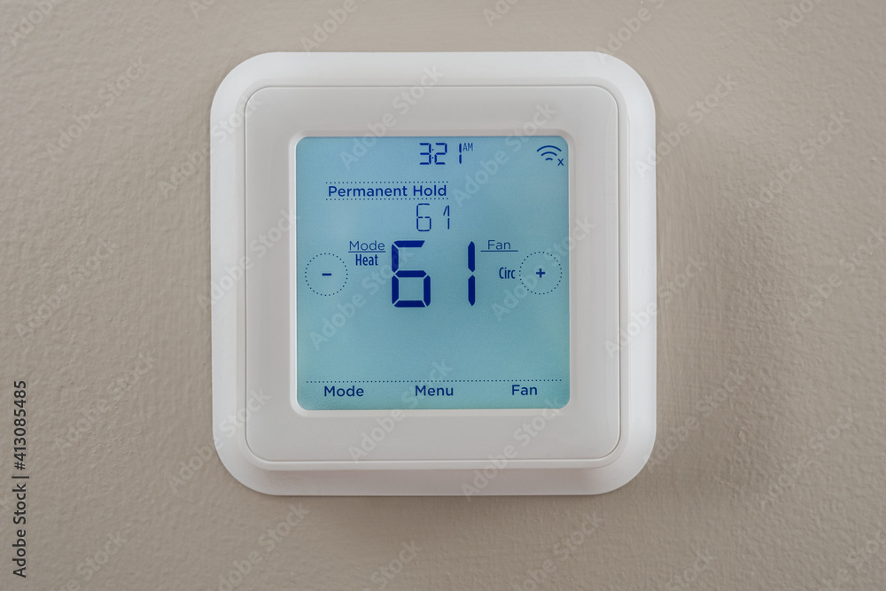 Photograph of a modern residential programmable heating and cooling thermostat mounted on a wall Photograph of a modern residential programmable heating and cooling thermostat mounted on a wall