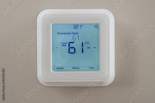 Photograph of a modern residential programmable heating and cooling thermostat mounted on a wall photo