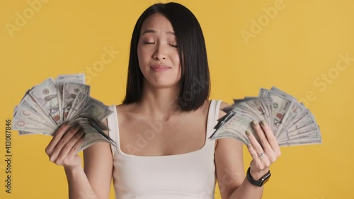 Beautiful stylish Asian girl looking confident waving wide of money on camera over colorful background. Successful concept