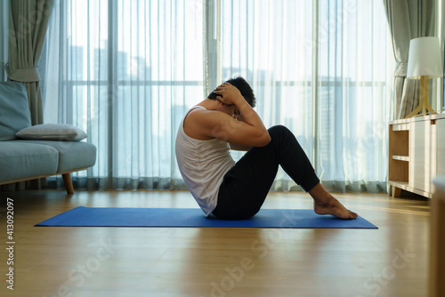 Asian man exercise at home by sit up during gym closures during COVID-19 outbreak.