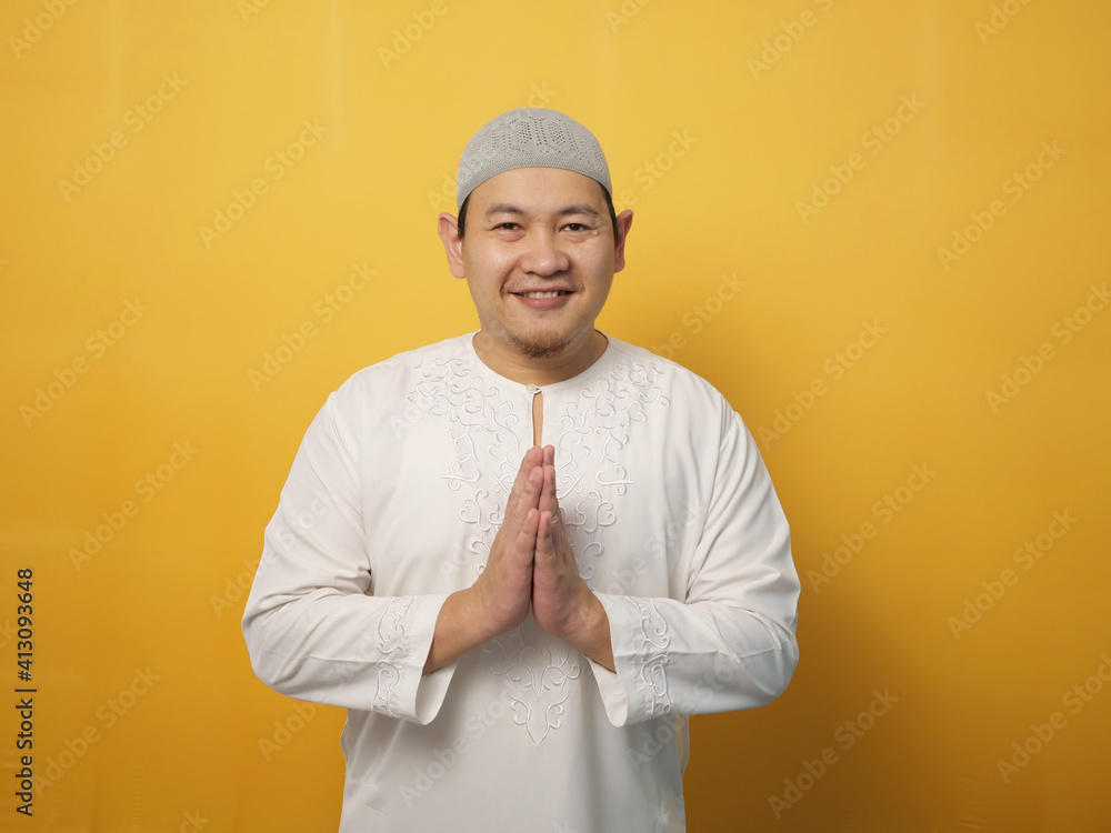 Asian muslim man smiling and shows greeting gesture against yellow background, concept of islamic celebration of ramadan or eid fitr Asian muslim man smiling and shows greeting gesture against yellow background, concept of islamic celebration of ramadan or eid fitr