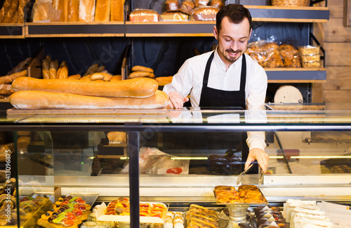 happy european male shop assistant demonstrating fresh delicious pastry in bakery