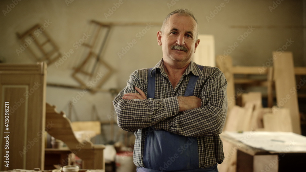 Obraz premium Positive man looking in camera indoors. Carpenter standing with crossed arms 