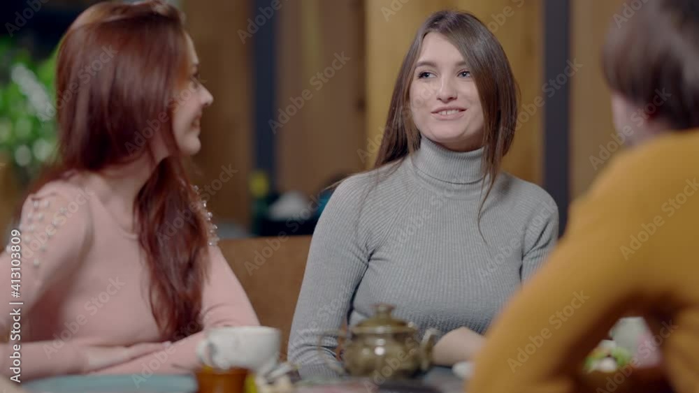 Middle shot of beautiful slim excited young woman talking with friends in cafe in slow motion. Portrait of Caucasian charming lady sitting in restaurant with positive millennials. Middle shot of beautiful slim excited young woman talking with friends in cafe in slow motion. Portrait of Caucasian charming lady sitting in restaurant with positive millennials.