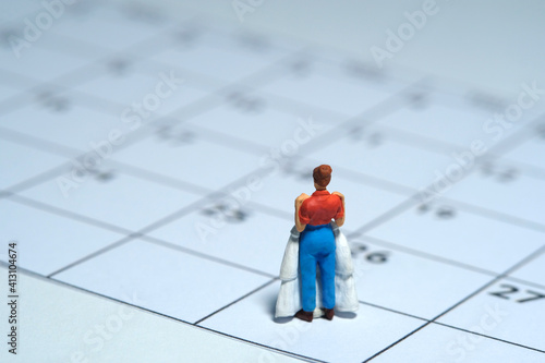 Woman miniature people stand above calendar while holding wedding dress, fitting day concept. Image photo © miniartkur
