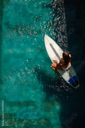 Photography Surf girl sit on surfboard in the swimming pool, top view